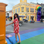 Woman in a red floral dress standing on a colorful pavement with a clock tower in the background.