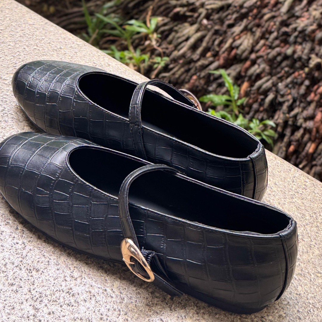 Black shoes with a textured pattern on a stone surface near water and plants.