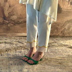Person wearing a light-colored outfit with green sandals on a textured floor.
