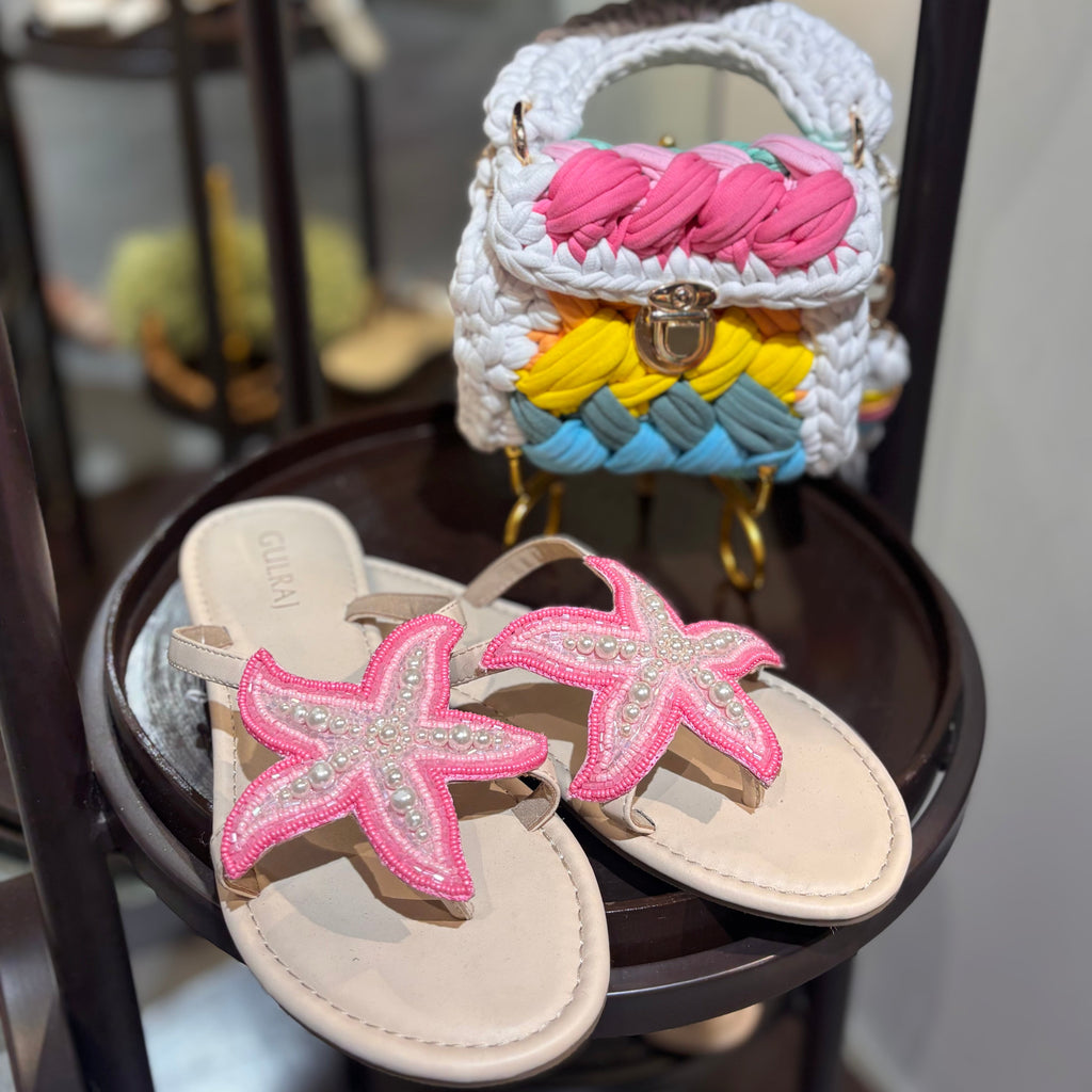 Pair of sandals with starfish design and a small handbag in the background.