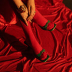 Person wearing red dress with green trim sitting on a red fabric surface
