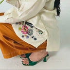Person wearing a white outfit with floral embroidery holding flowers on a plain background