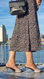 Woman in a black and white patterned skirt with metallic heeled sandals and black handbag by waterfront