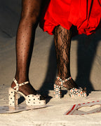 Person wearing polka dot shoes and black lace stockings on a textured surface.