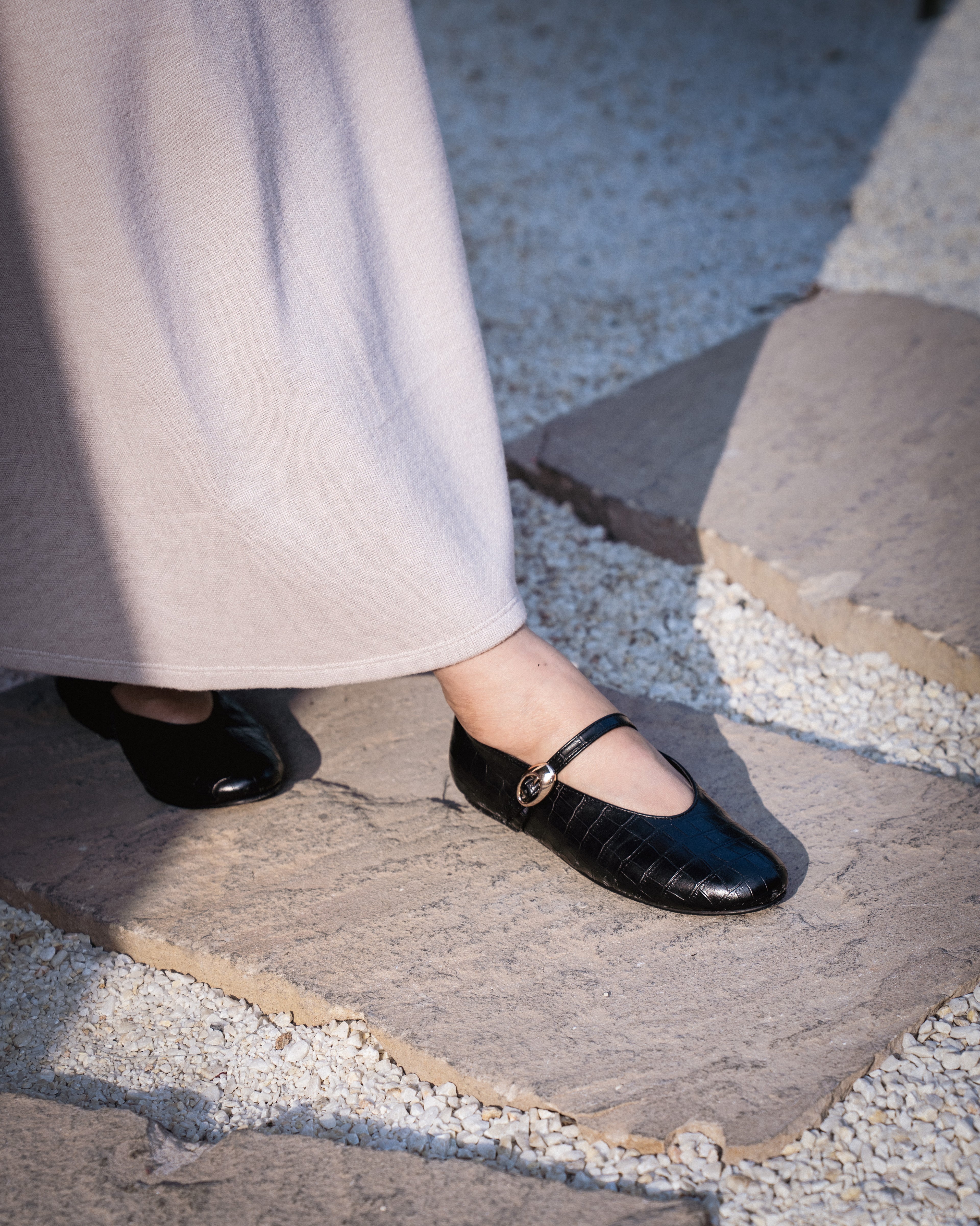 Person wearing black shoes on a stone path..  minimal ballet flats India
