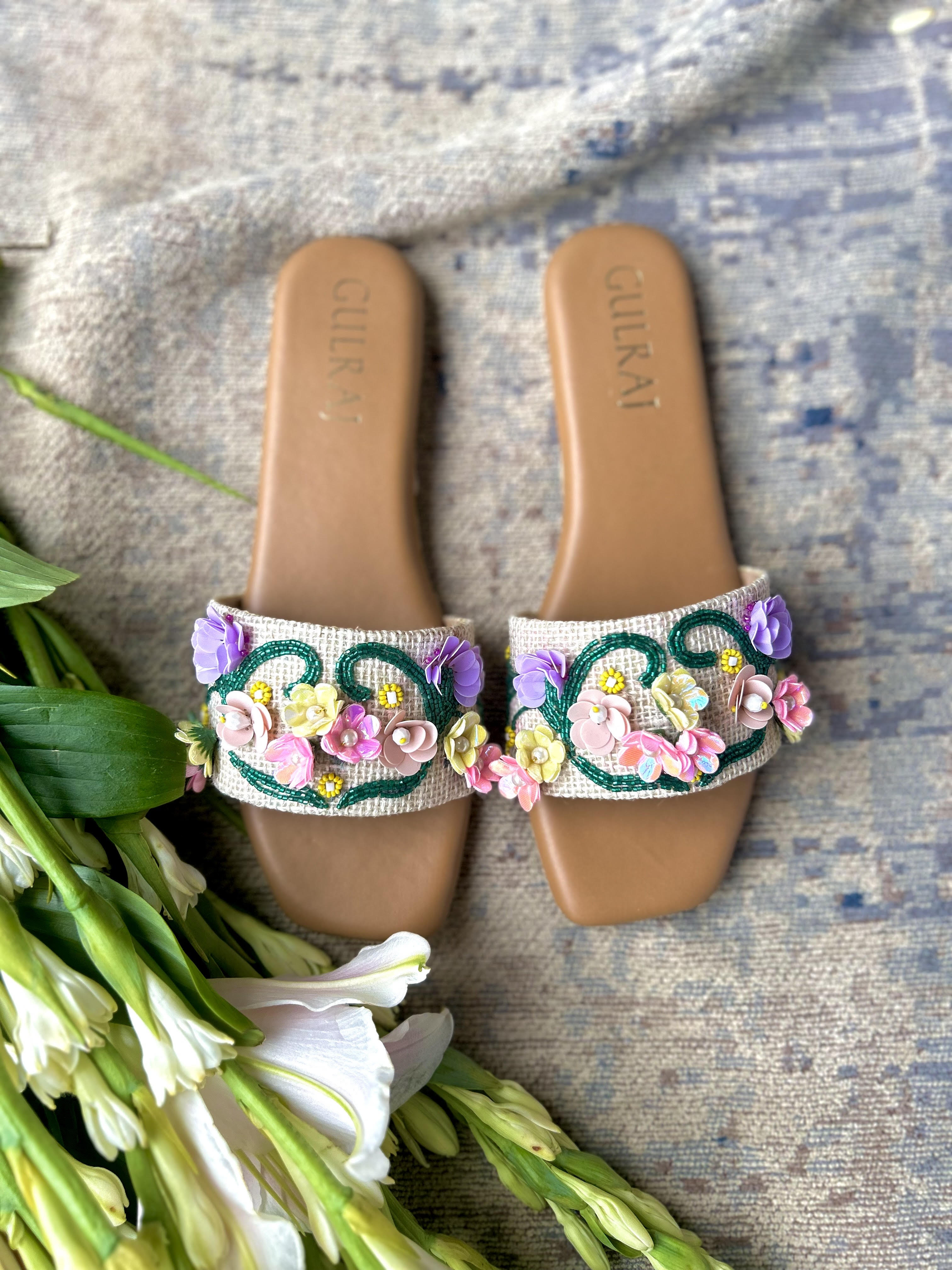 Pair of embellished sandals with floral designs on a textured surface with flowers.