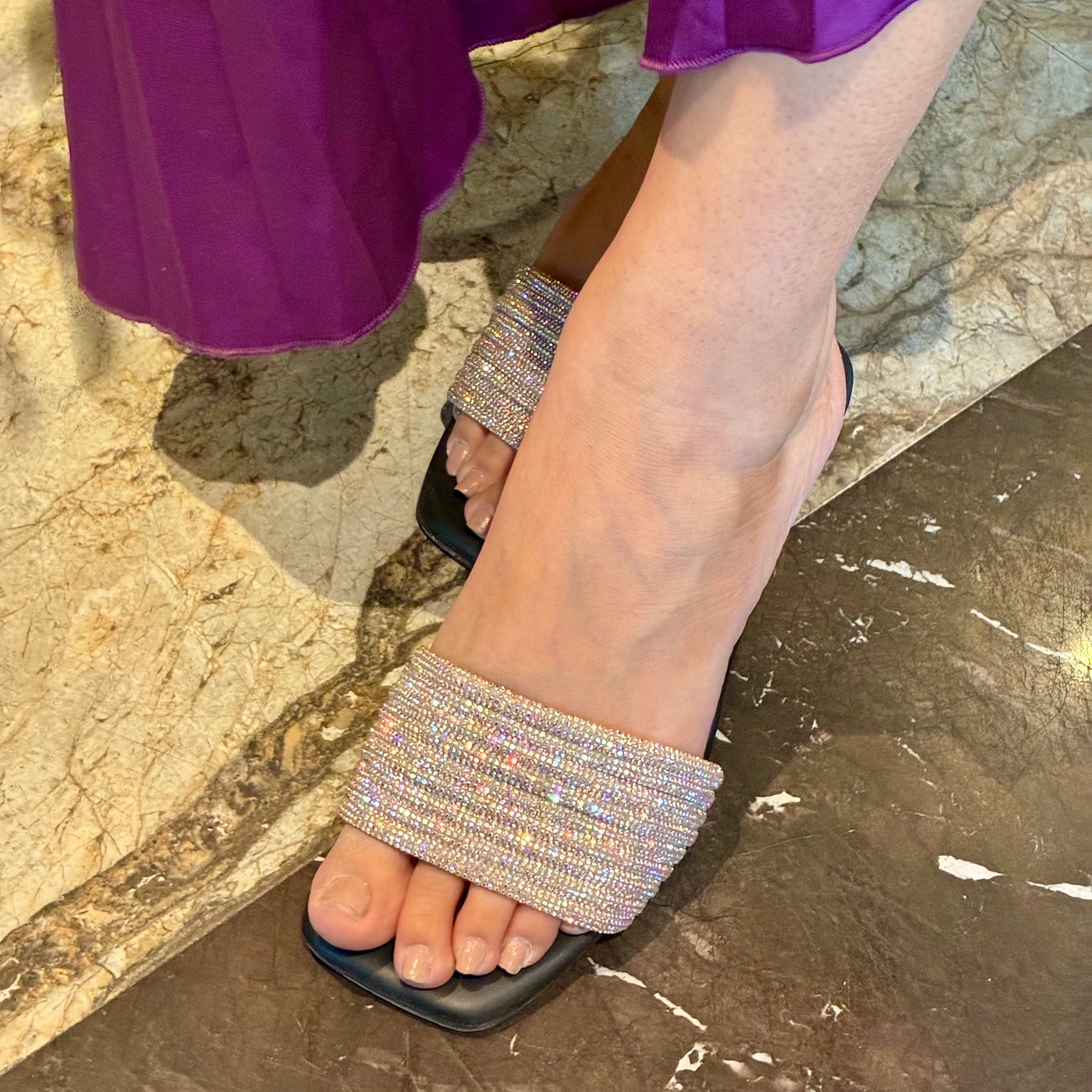 Person wearing a sparkling sandal on a stone surface with a purple skirt.
