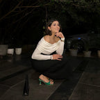 Woman in a white top and black skirt sitting on a stone floor with dark background
